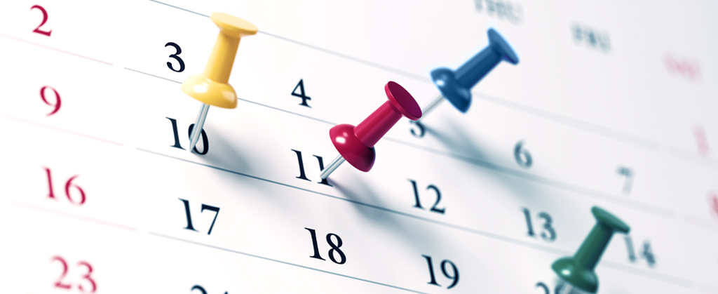 Ausschnitt aus einem Kalenderblatt mit farbigen Pins, die in einzelnen Datumsfeldern stecken