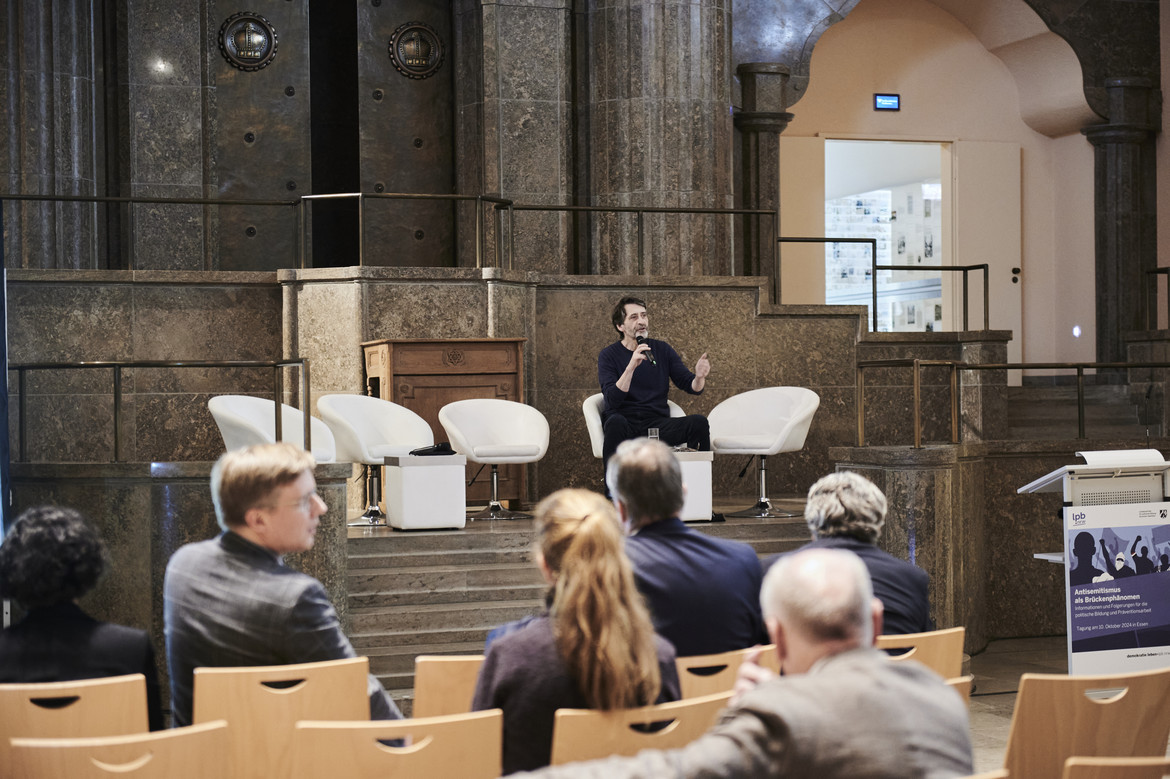 Prof. Dr. Armin Pfahl-Traughber sitzend mit Mikrofon in der Hand vor Publikum