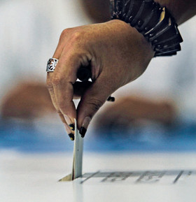 Hand wirft Stimmzettel in Wahlurne.
