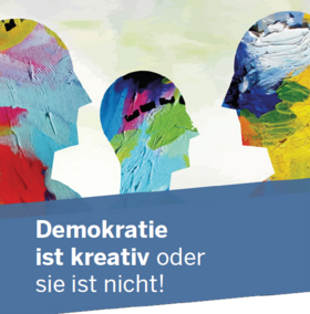 Das Bild zeigt stilisierte, farbenfroh bemalte Köpfe vor einem hellen Hintergrund. Darunter steht der Schriftzug "Demokratie ist kreativ oder sie ist nicht!" auf einem blauen Banner.
